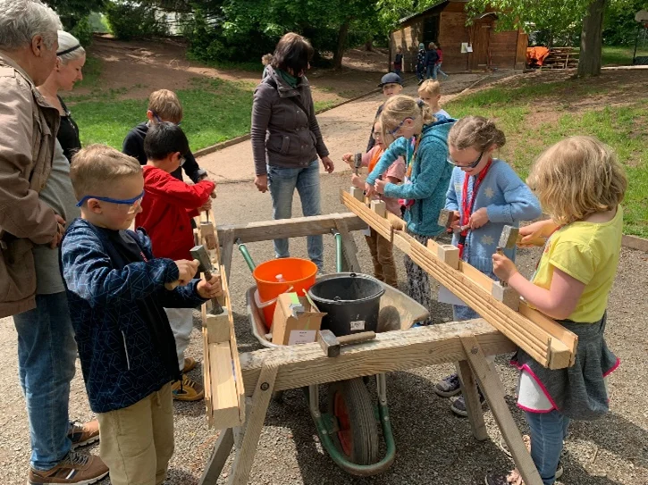 Kinder stehen um einen Tisch und arbeiten mit Holz
