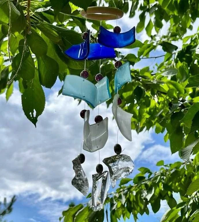 Windspiel aus blauen, türkisen und transparenten Glasfiguren an einem Baum